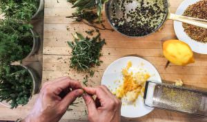 hands pinching at herbs next to a plate with lemon zest and ingredients in a pot