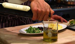 Jordan Winery extra virgin olive oil being poured into beaker with chopped ingredients on plate in background