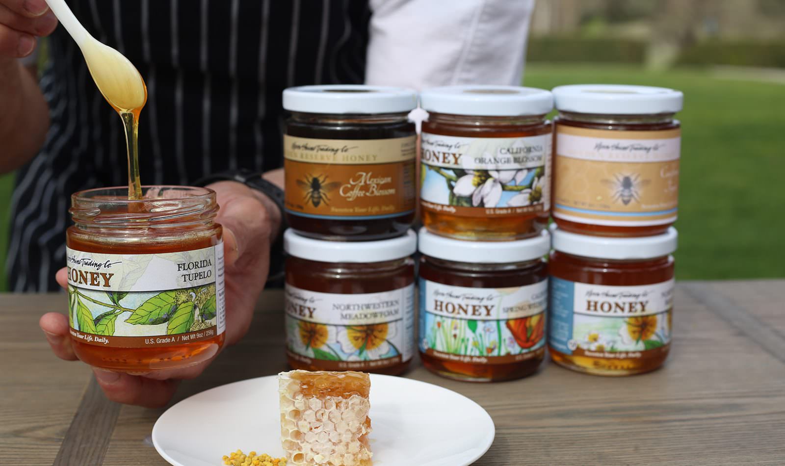 hands holding an open jar of honey next to other jars of honey