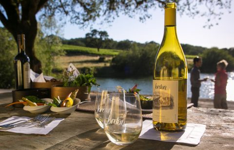 bottle of Jordan Winery Chardonnay with two logo glasses and bites of food on the Jordan Winery property