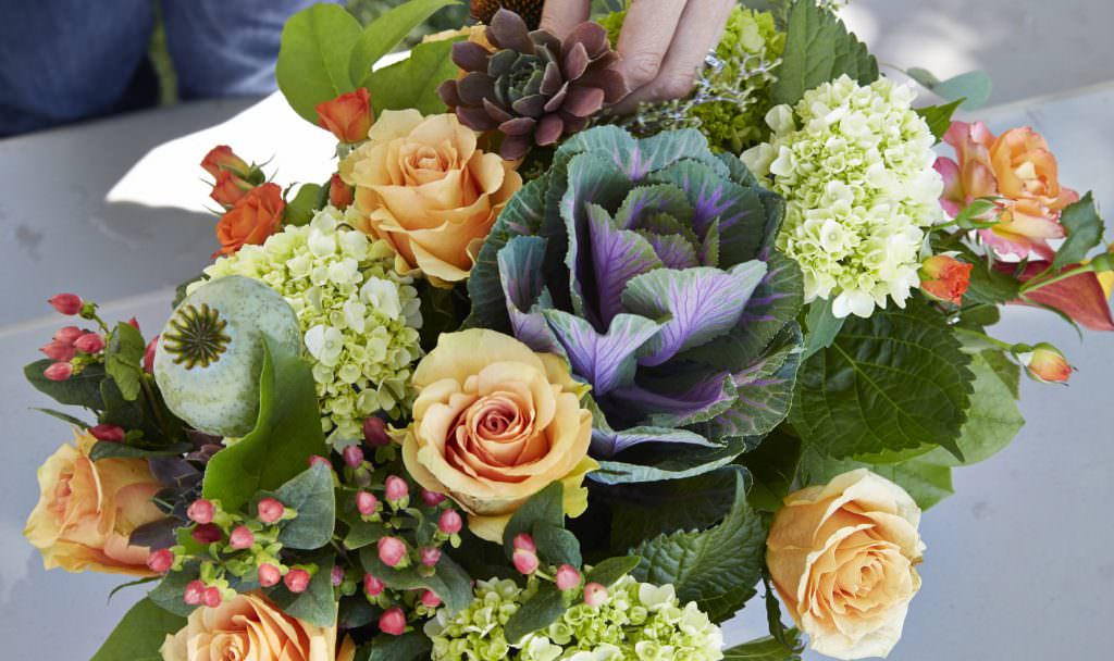 A floral arrangement with ornamental cabbage, smooth hydrangea, orange spray roses and orange flame calla lily.