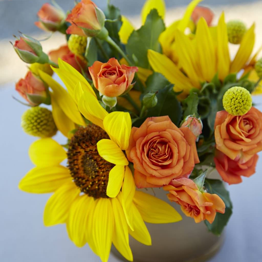 Flower centerpiece with sunflowers and orange spray roses.