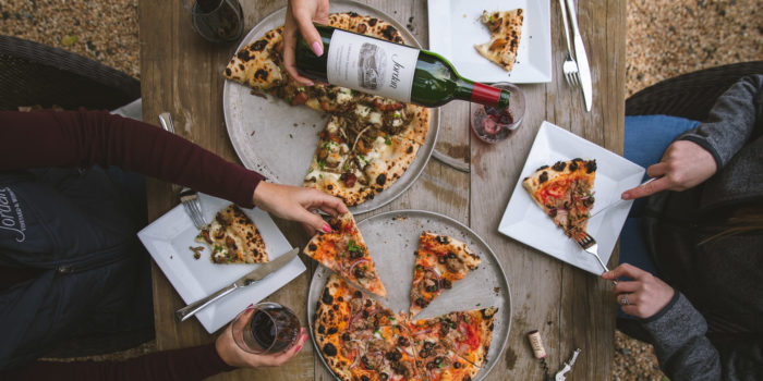 overhead shot of two people sitting at a table with pizza and Jordan winery Cabernet being poured into a glass