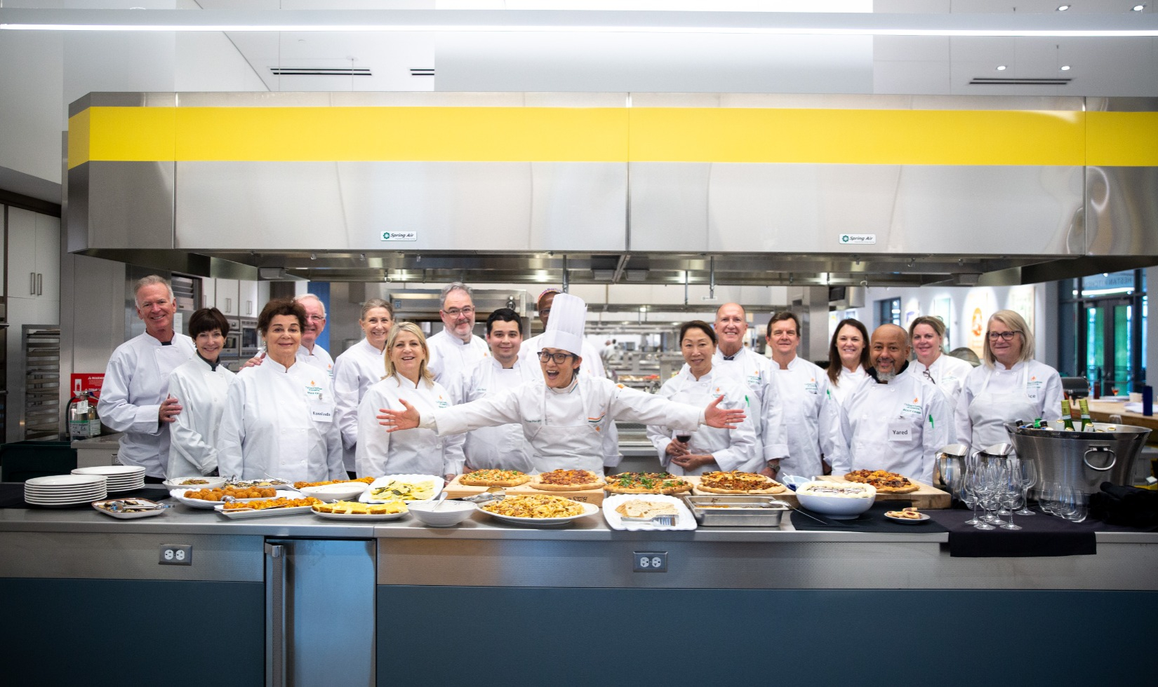 Group cooking class in commercial kitchen with everyone in white uniforms.
