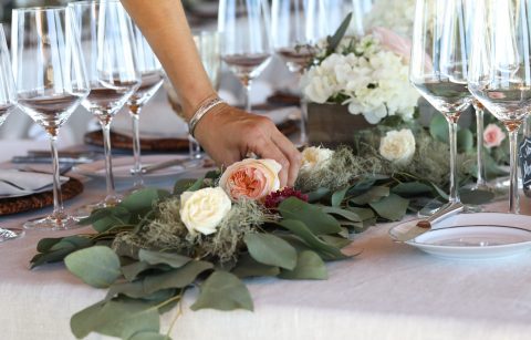 hand adjusting a eucalyptus garland table runner on a dining table