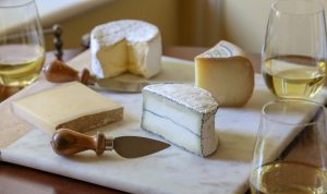 four different types of cheese on a cheese board next to poured glasses of Chardonnay