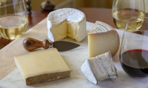 four different types of cheese on a cheese board next to poured glasses of wine