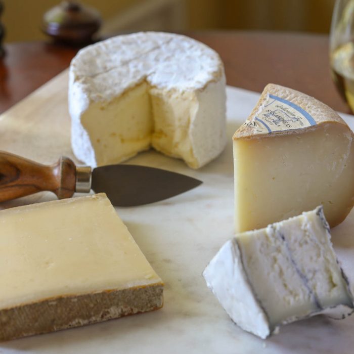 four different types of cheese on a cheese board next to poured glasses of wine