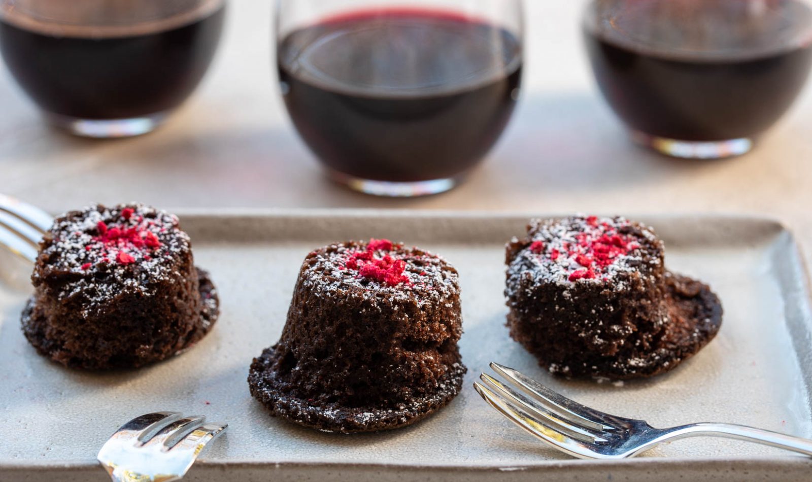 three Jordan Winery red wine chocolate cakes on a plate with red wine in glasses in the background