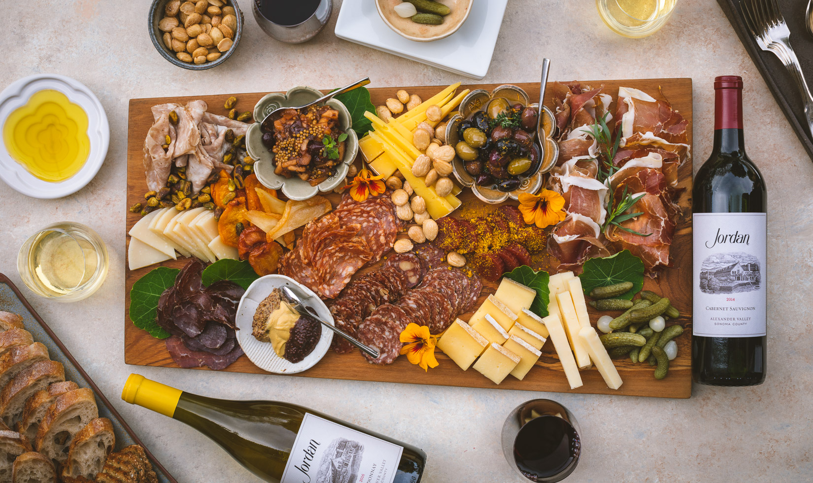 large charcuterie and cheese board with olives, pickles and marcona almonds and Jordan Cabernet and Chardonnay