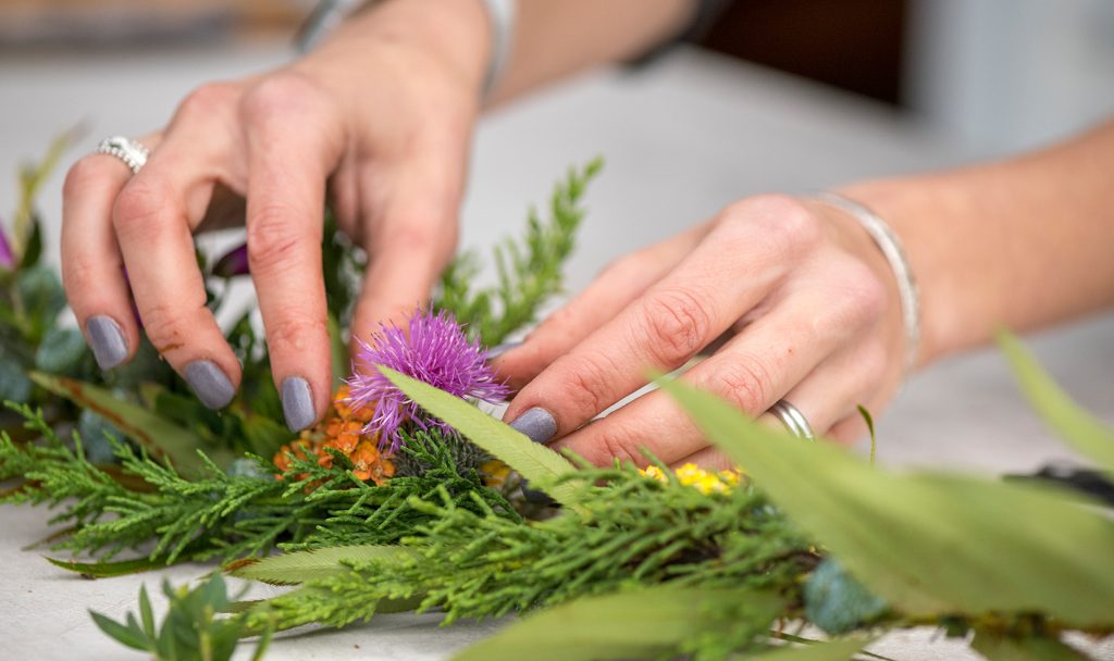 Close-up image of hands placing a pink flower into a table garland.