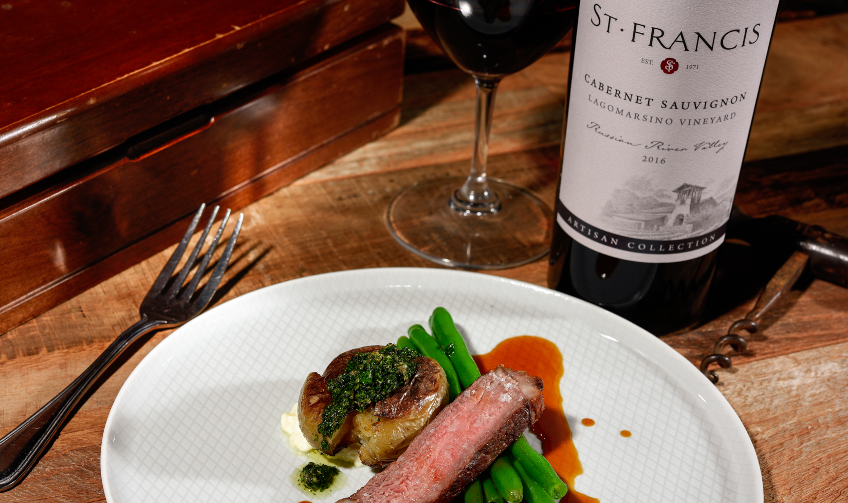 cut of steak and green beans on dinner plate with bottle of wine