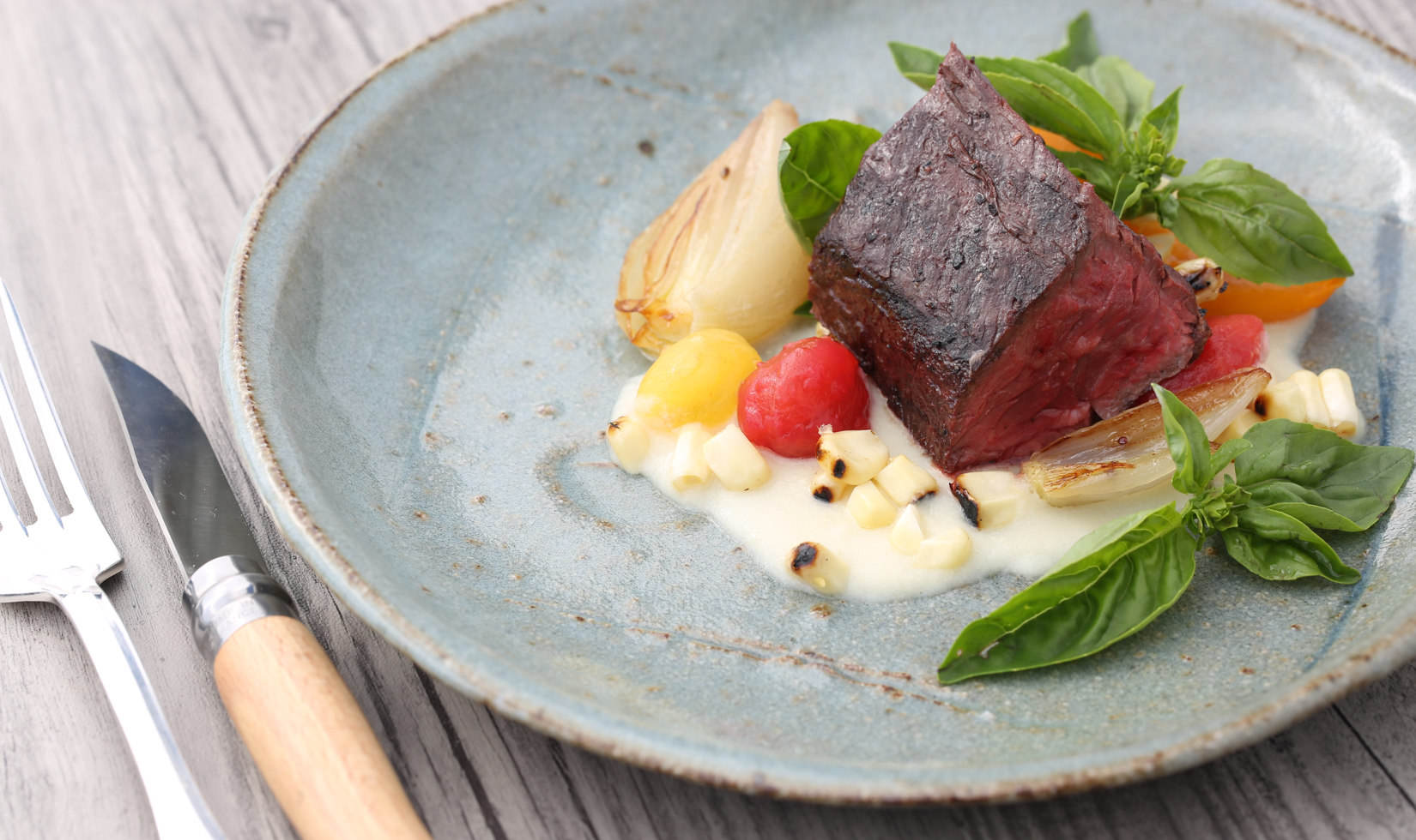 Jordan Winery Wagyu Steak with Heirloom Tomato and Corn Pudding on blue plate with utensils 