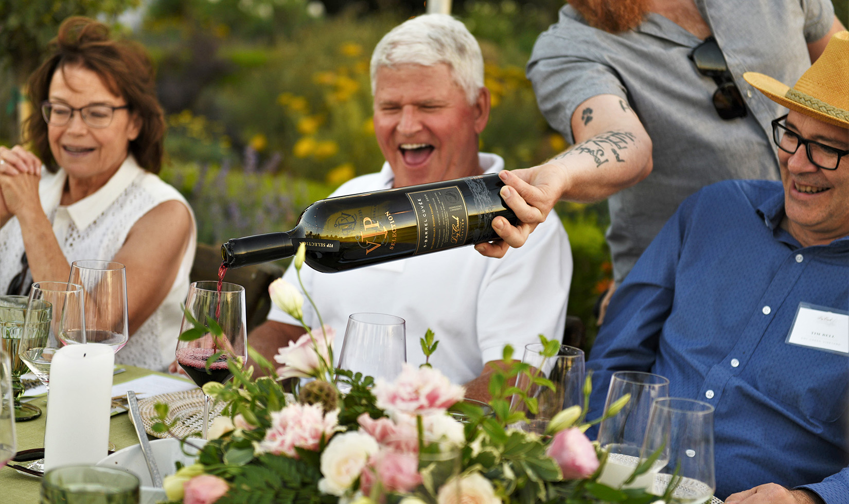 server pouring red wine into a glass with three happy people in the background