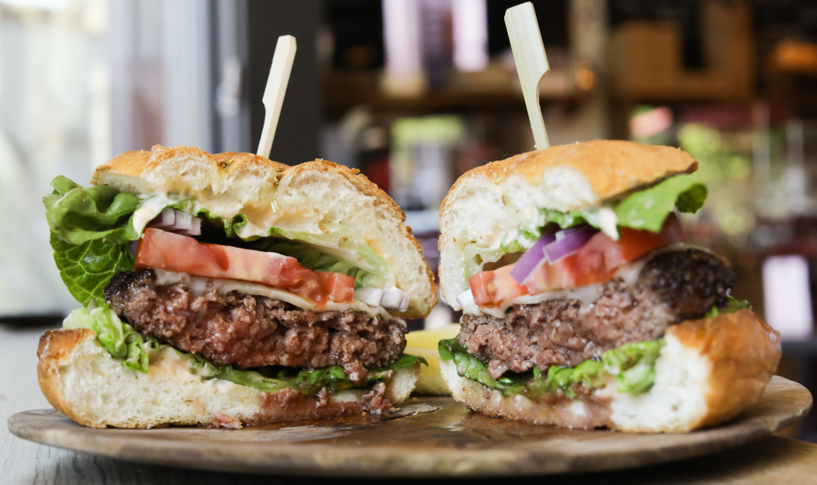 cheeseburger cut in half on wooden plate with lettuce and tomatoes