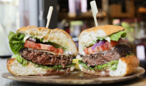 cheeseburger cut in half on wooden plate with lettuce and tomatoes