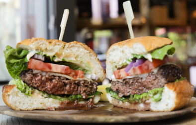 cheeseburger cut in half on wooden plate with lettuce and tomatoes