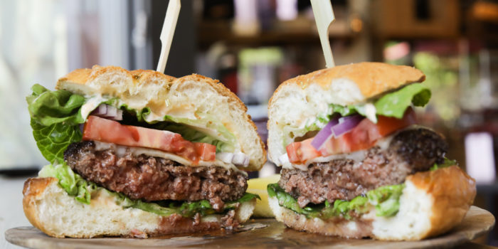 cheeseburger cut in half on wooden plate with lettuce and tomatoes