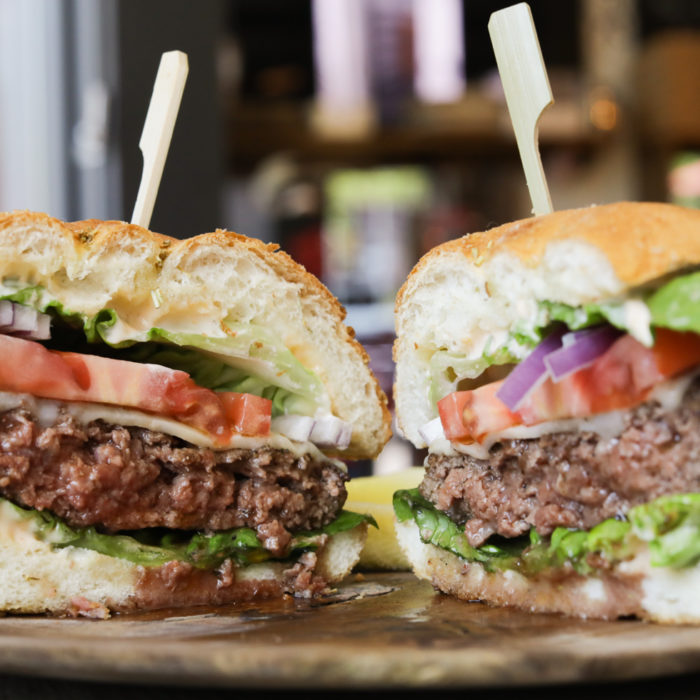 cheeseburger cut in half on wooden plate with lettuce and tomatoes