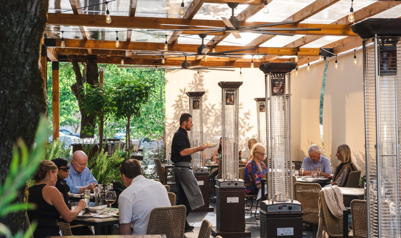 Diners enjoying meals on the patio at Valette restaurant with heat lamps by the tables and outdoor shades enclosing the space