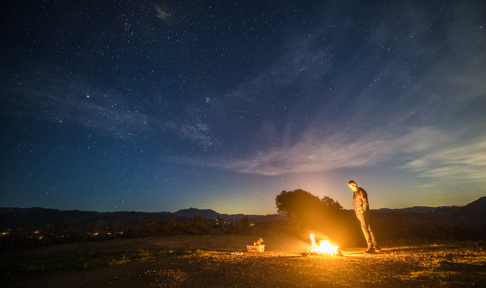 man standing in a field with a fire in front of him