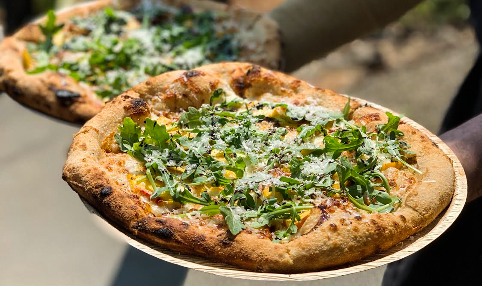 Outdoor Wine Tastings person holding two wood-fired pizzas