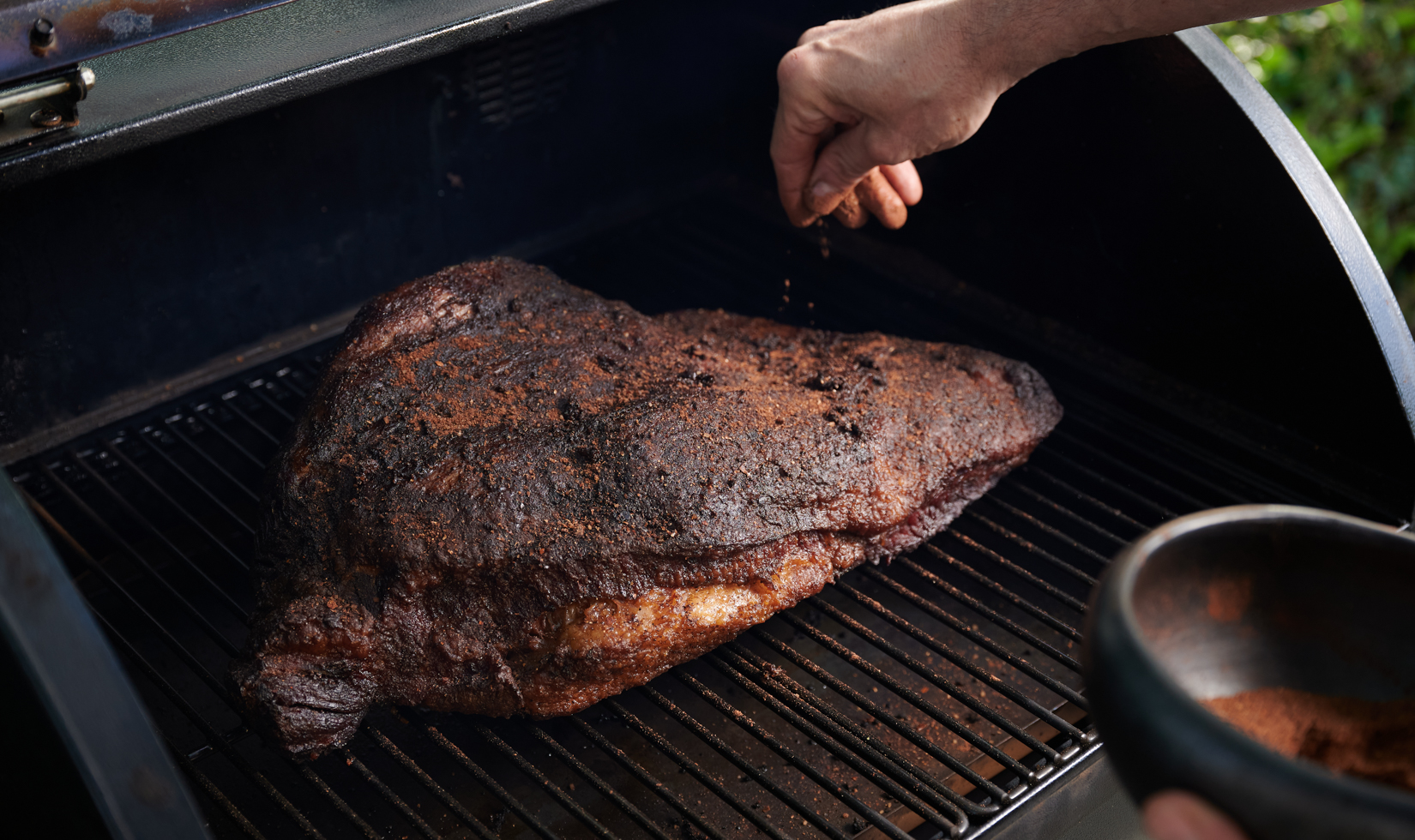 Food Pairing with Cabernet Sauvignon hand sprinkling spice on large brisket on grill
