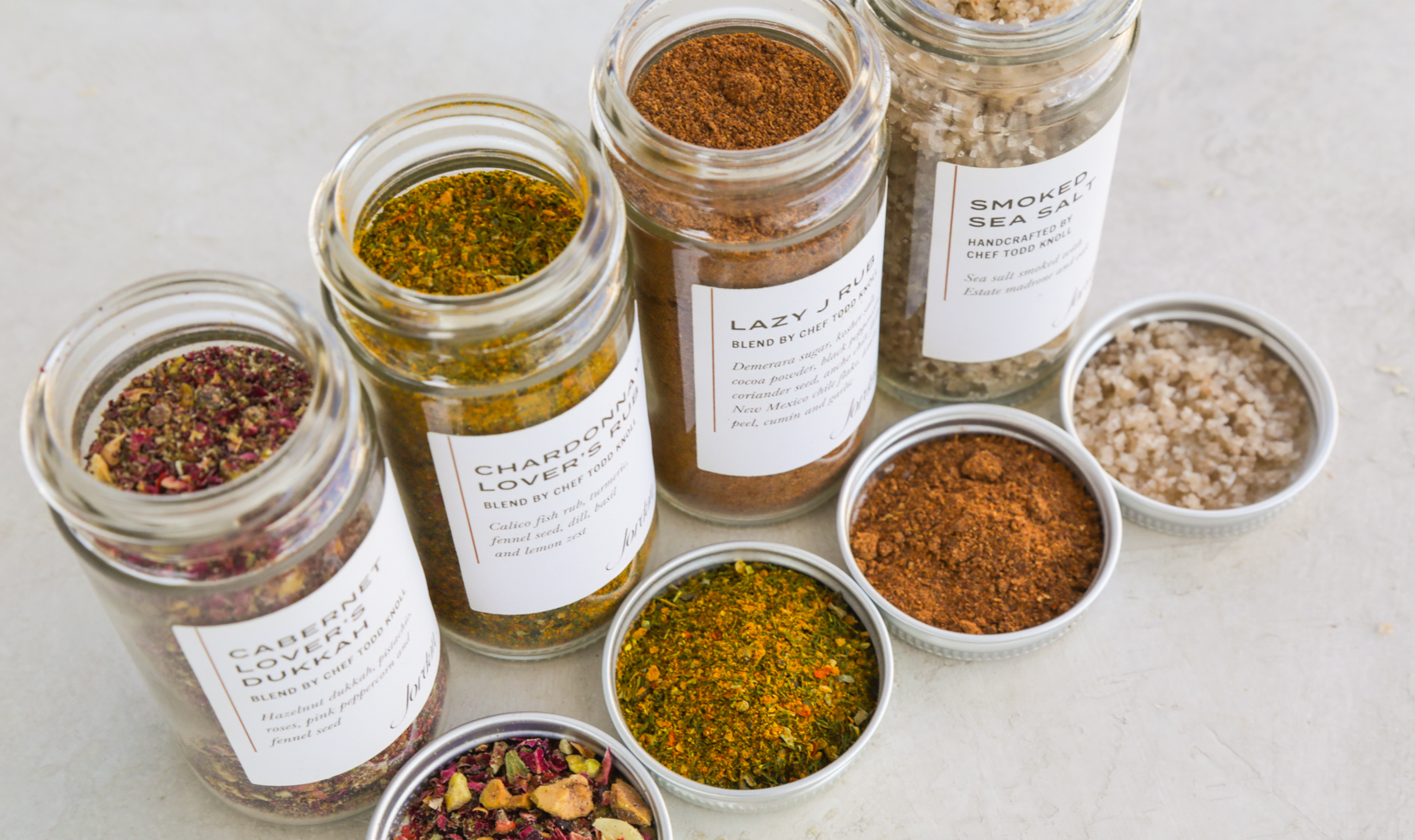 four spice blends in glass jars on white surface