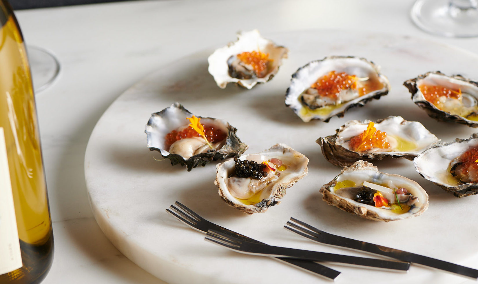 oysters with salmon roe on white marble plate next to bottle of chardonnay