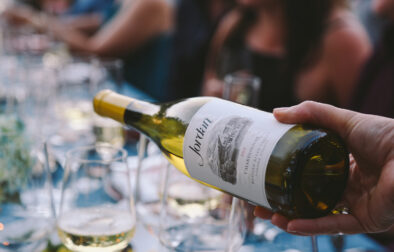 a person pouring a white wine to a glass in a table full of guests as featured in wine country table.