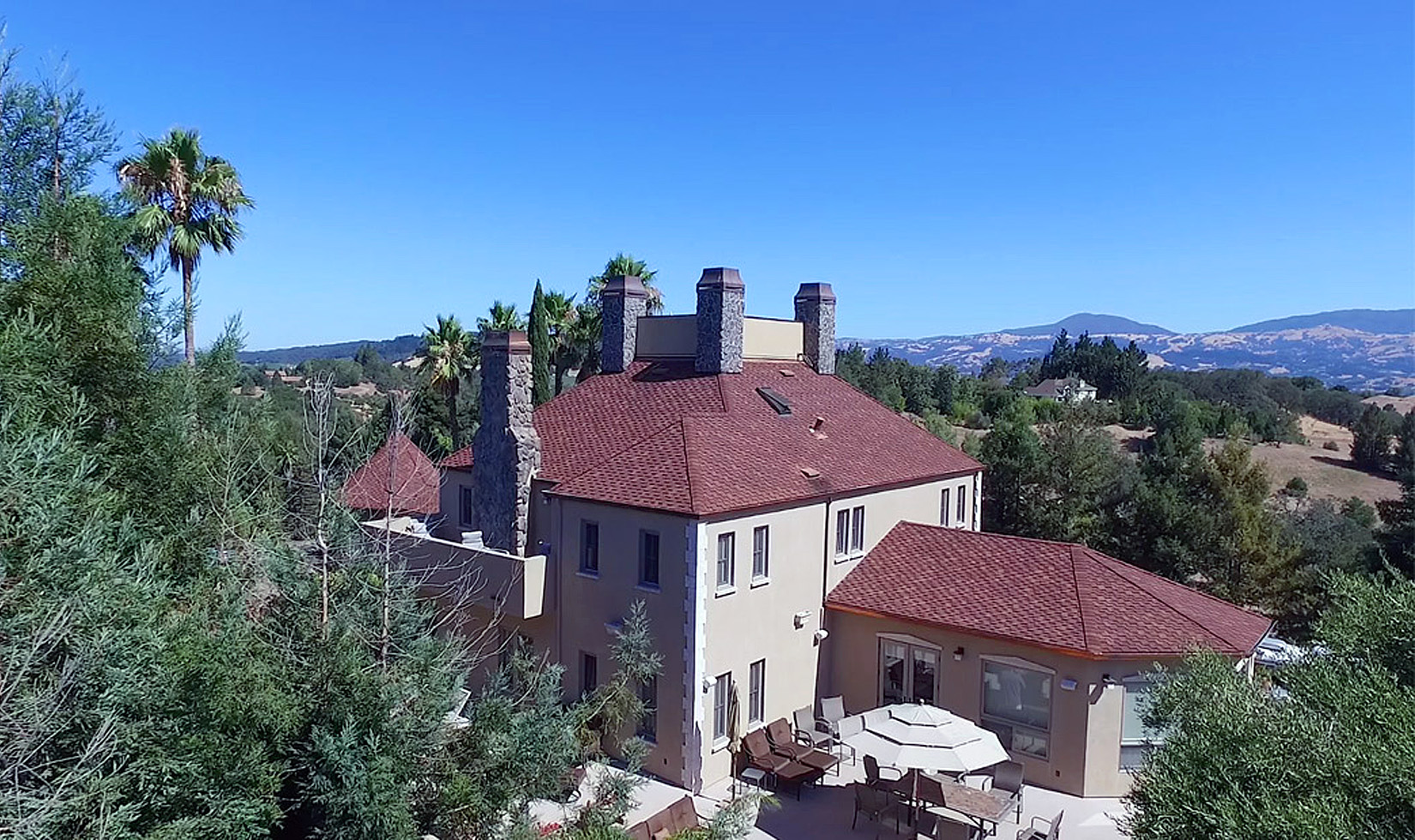 Luxury estate with red roof, stone chimneys, and scenic hillside views.