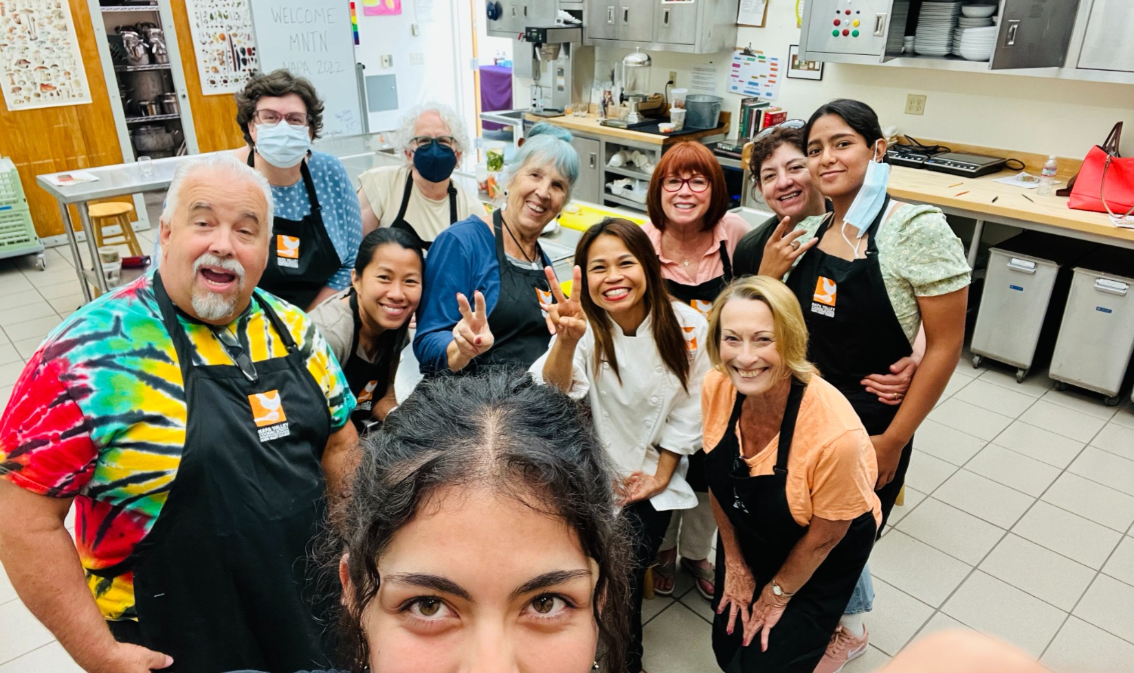 Group of cooking students posed for photo in commercial kitchen all wearing black aprons.