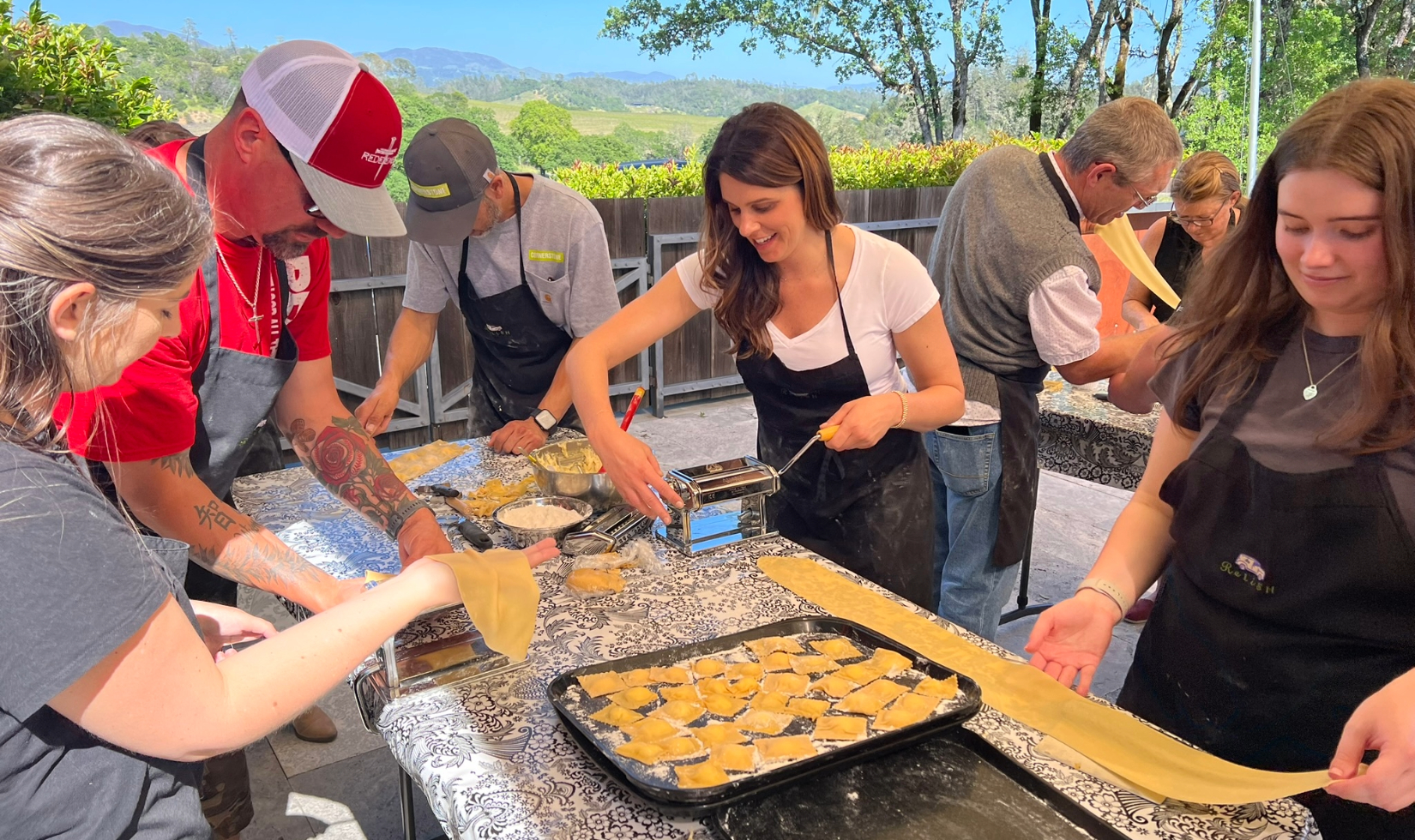 group in cooking class making ravioli pasta around table on terrace overlooking hills