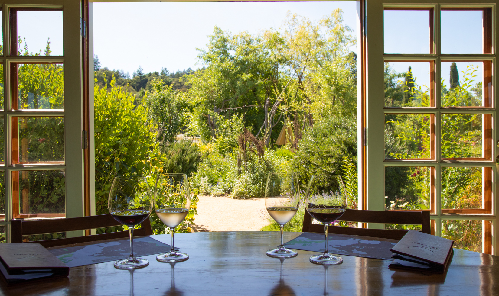 four wine glasses filled with rose and red wine on a table with garden views