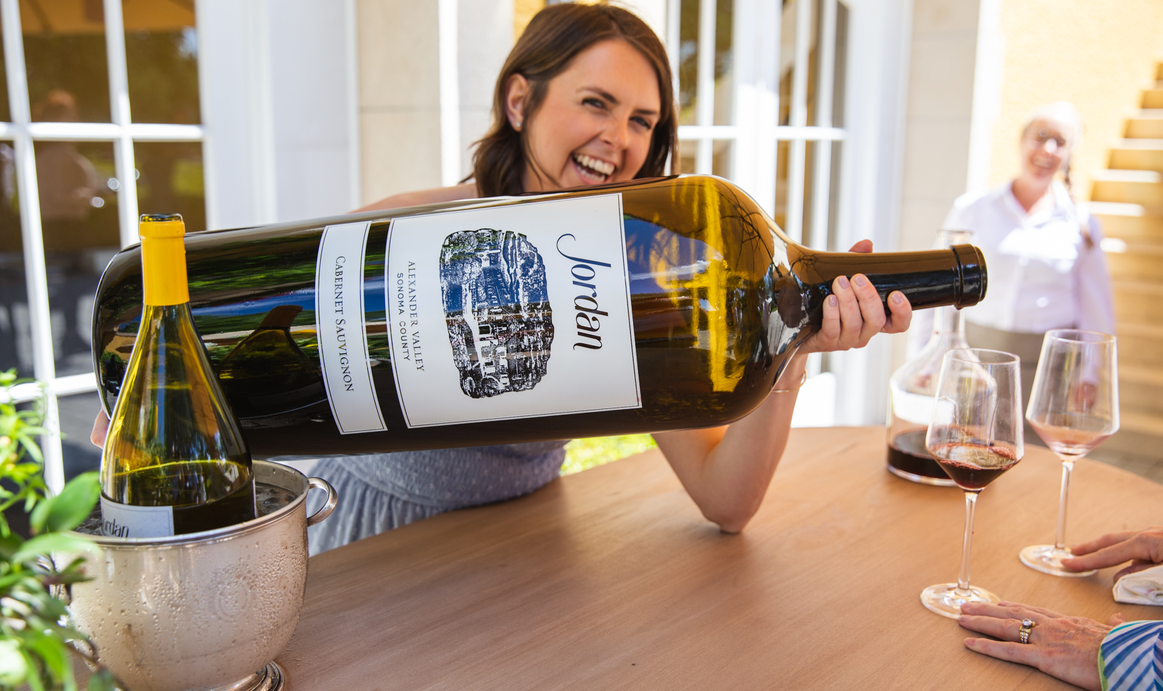 woman pouring out of a large bottle of cabernet sauvignon at a party