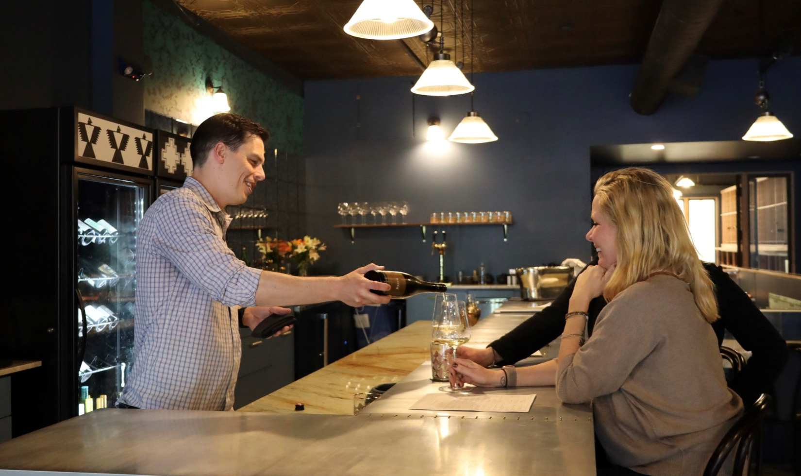 bartender pouring a glass of red wine for two guests at the bar at Maison Wine Bar