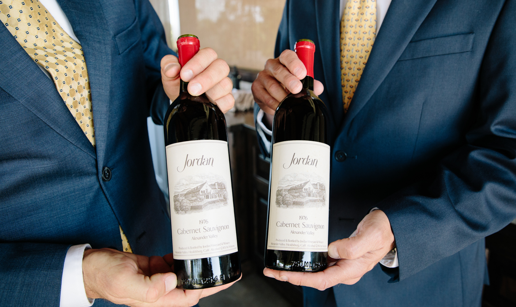 two men in blue suits holding two bottles of old cabernet bottles