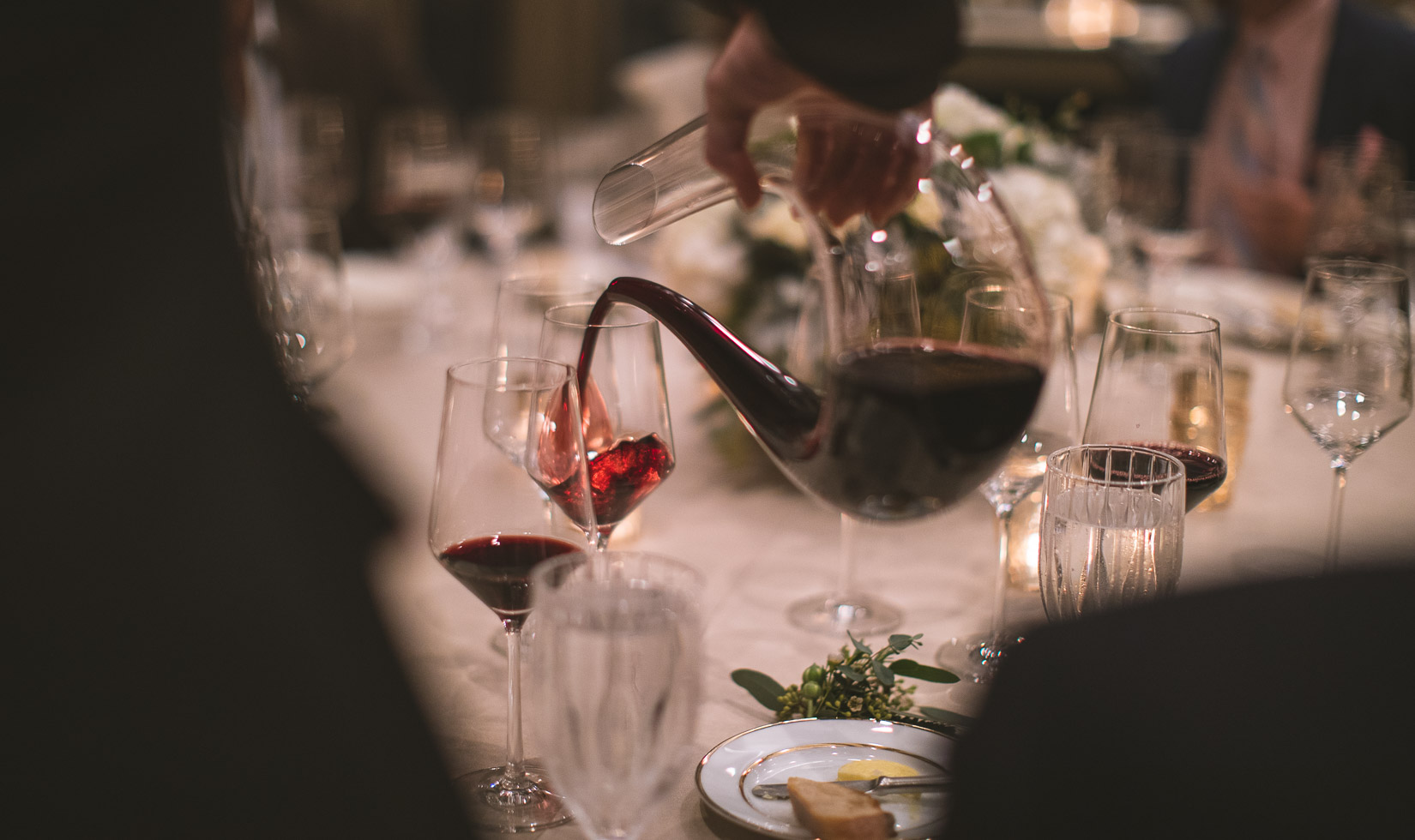 glass decanter pouring cabernet into wine glasses on formal dining table