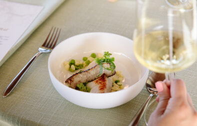 close up of halibut dinner dish inside a white bowl with a glass of white wine