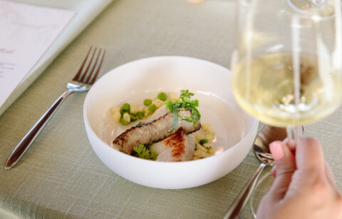 close up of halibut dinner dish inside a white bowl with a glass of white wine