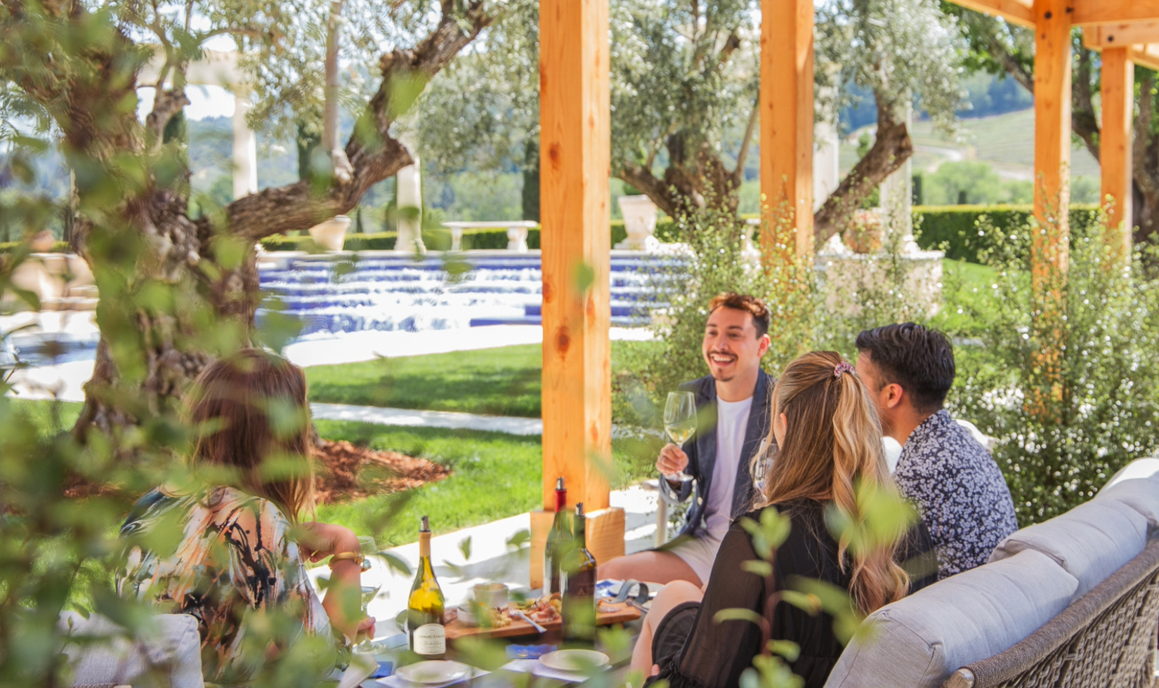 Group sitting under pergola around table set for a wine tasting