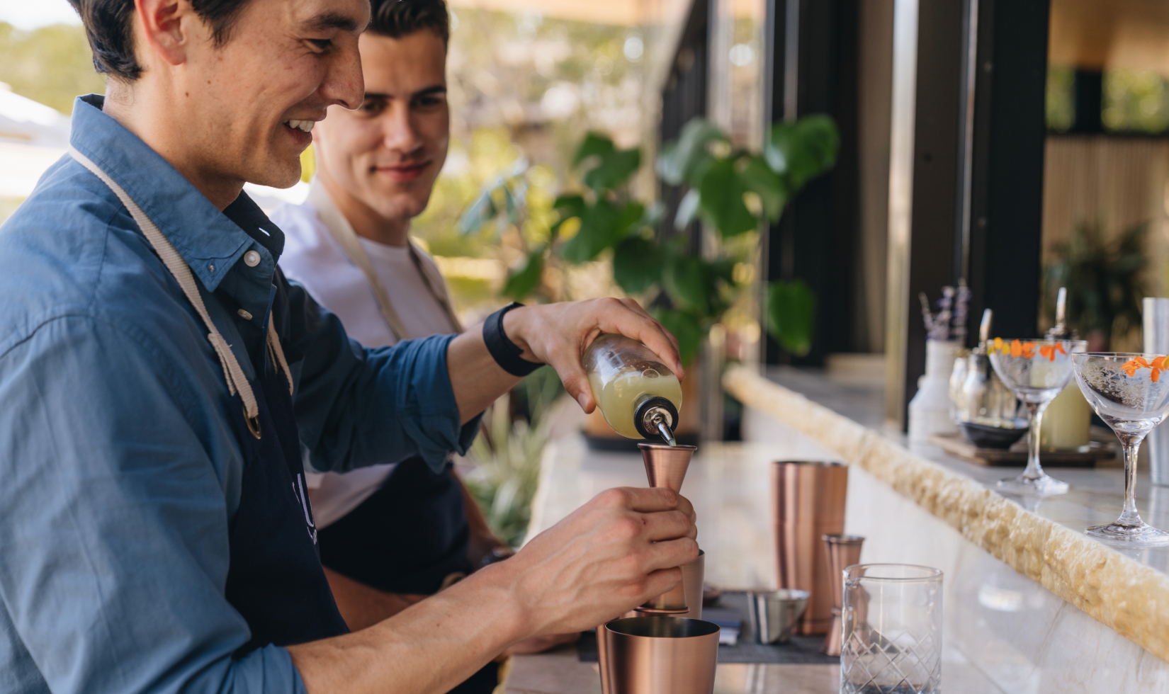 Two bartenders making drinks behind a bar
