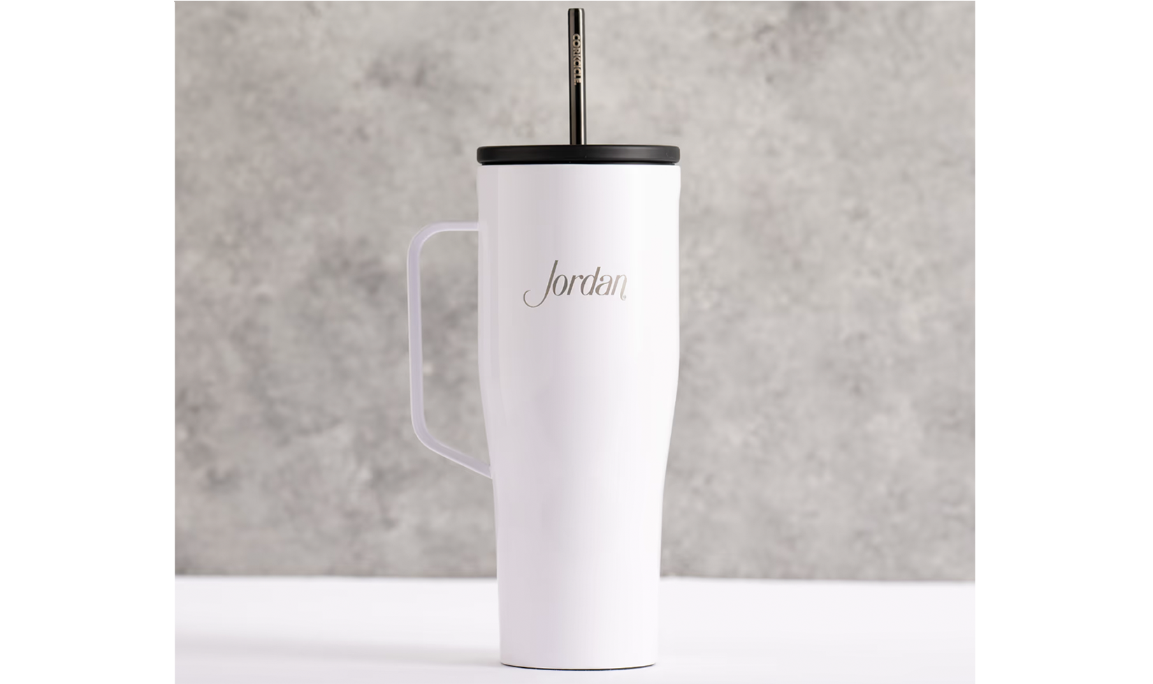 White tumbler with handle, black lid, and straw, featuring "Jordan" engraving.